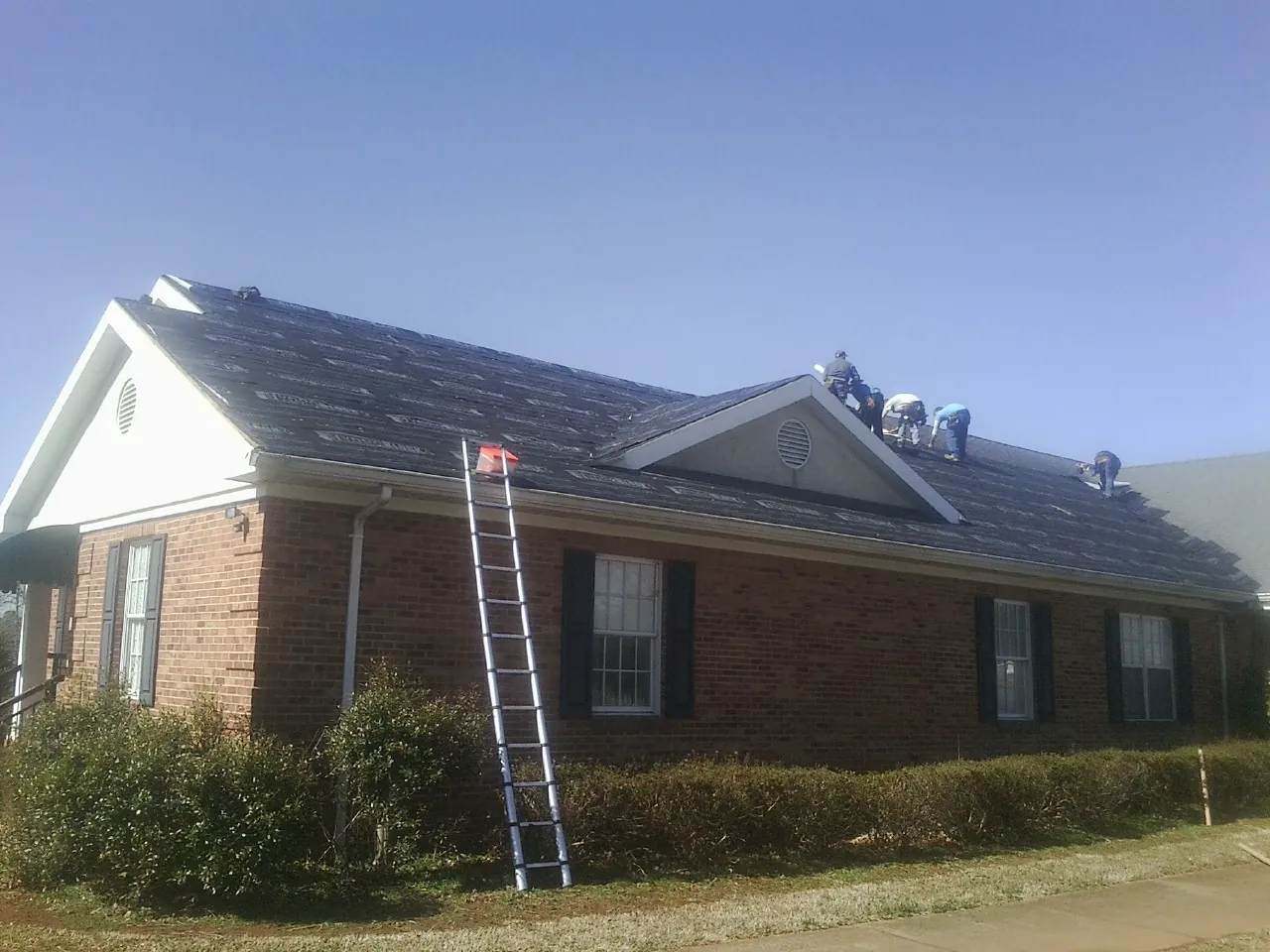 Crew tearing shingles off a brick ranch roof with a ladder set — Metal Roof Repair work by our crew in Gilmanton Iron Works