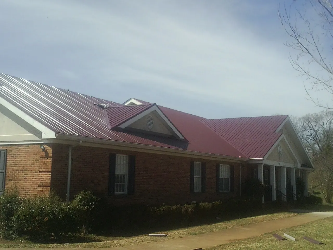 Red metal roof with gabled entries on a long brick building, from a Hail Damage Roof Repair job in Gilmanton Iron Works