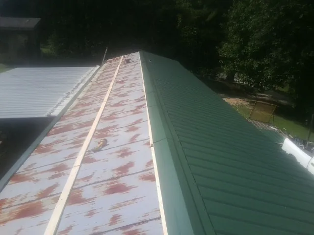 Old rusted panels beside newly installed green metal roofing in Gilmanton Iron Works