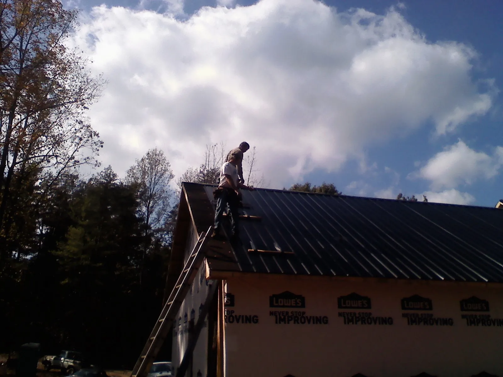 Roofer fastening dark metal panels high against a cloudy sky, from a Roof Inspection job in Gilmanton Iron Works