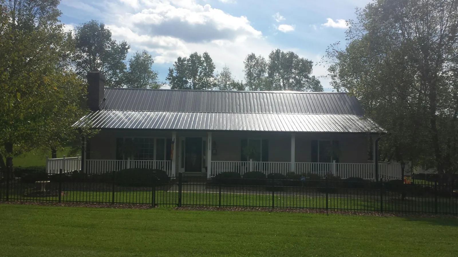 Gray metal roof on a brick ranch with a full width front porch — Gutter Guard Installation work by our crew in Gilmanton Iron Works