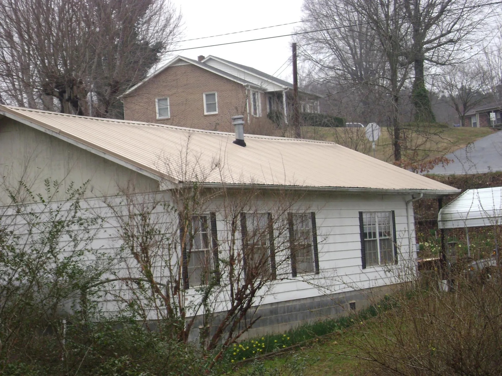 Tan metal roof on a white sided house set into a hillside — Commercial Roofing by Roofing Brothers in Gilmanton Iron Works