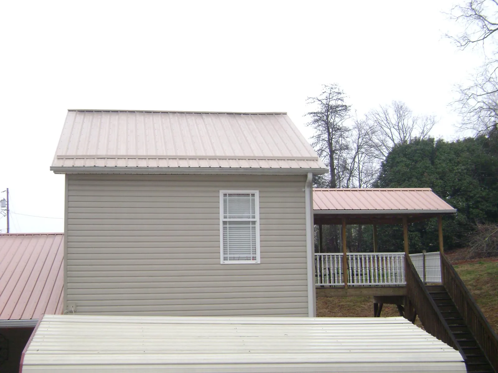 Tan metal roofs on a two story addition and attached porch, from a Roof Replacement job in Gilmanton Iron Works